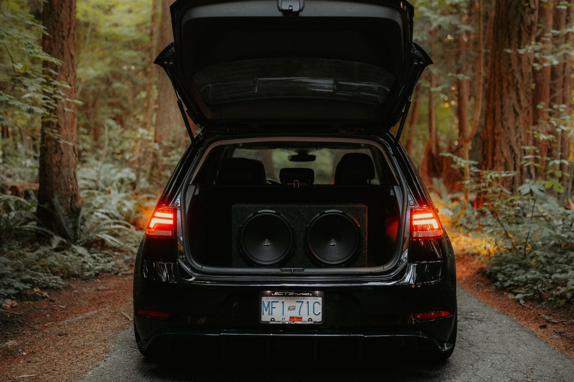 Car with trunk open showing large subwoofer speakers mounted inside for car audio